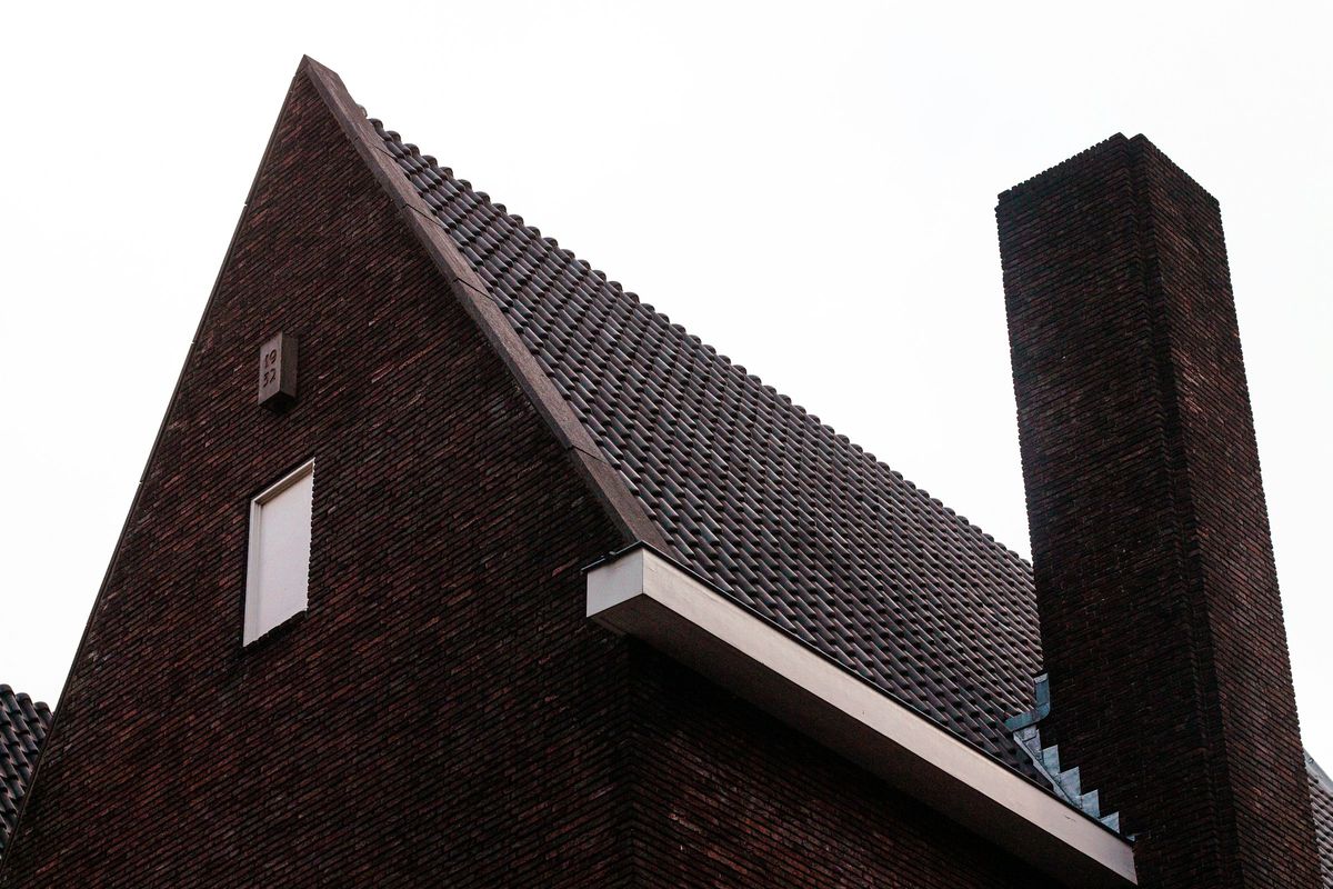 Puntgevel van een oudere woning in donkere baksteen met een hoge schoorsteen