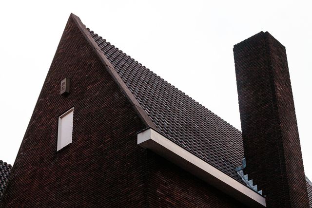 Puntgevel van een oudere woning in donkere baksteen met een hoge schoorsteen