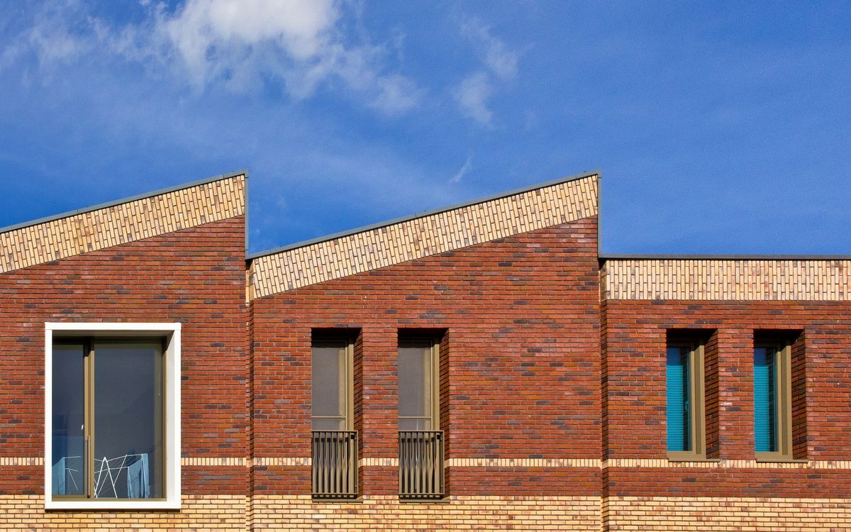 Hedendaagse woningen in rode en gele baksteen met schuine daklijnen onder een blauwe lucht
