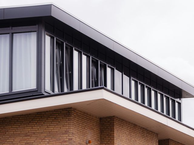 Een nieuwe verdieping met donkere gevelplaten op een gebouw in gele baksteen