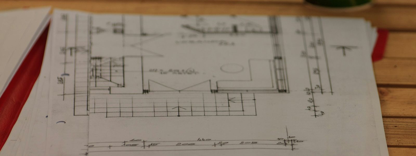 Getekende bouwplannen met maten in centimeter op een houten tafel