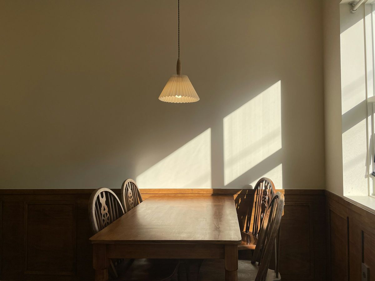 Zonlicht valt door een raam op de muur boven een houten eettafel met stoelen